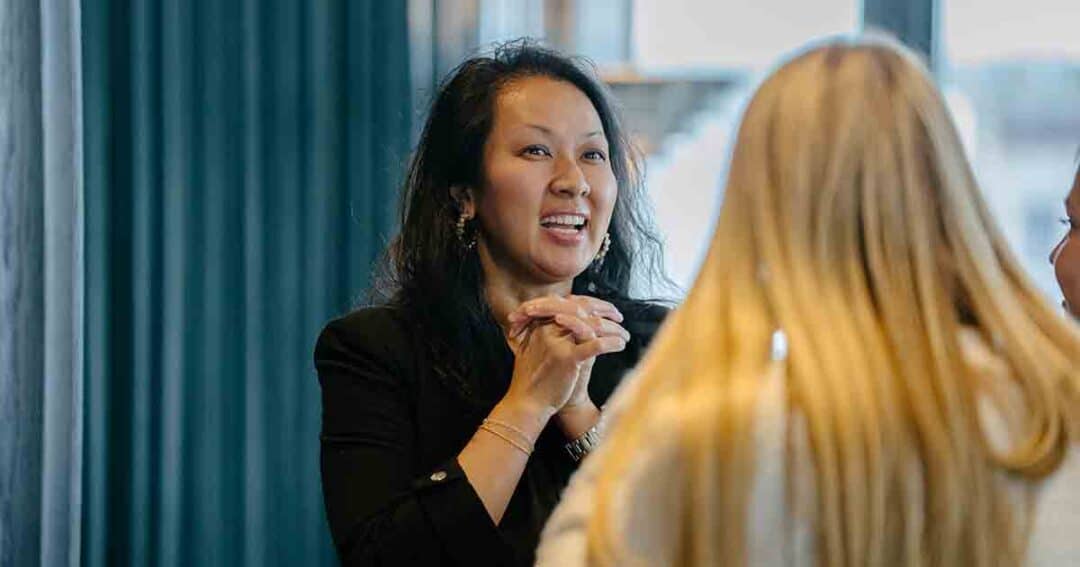 Allergy & Asthma Day Capitol Hill 2025: Leading the Charge Amid Federal Policy Shifts 31 A woman with dark hair smiles and clasps her hands while talking to two blonde women in a brightly lit indoor setting.