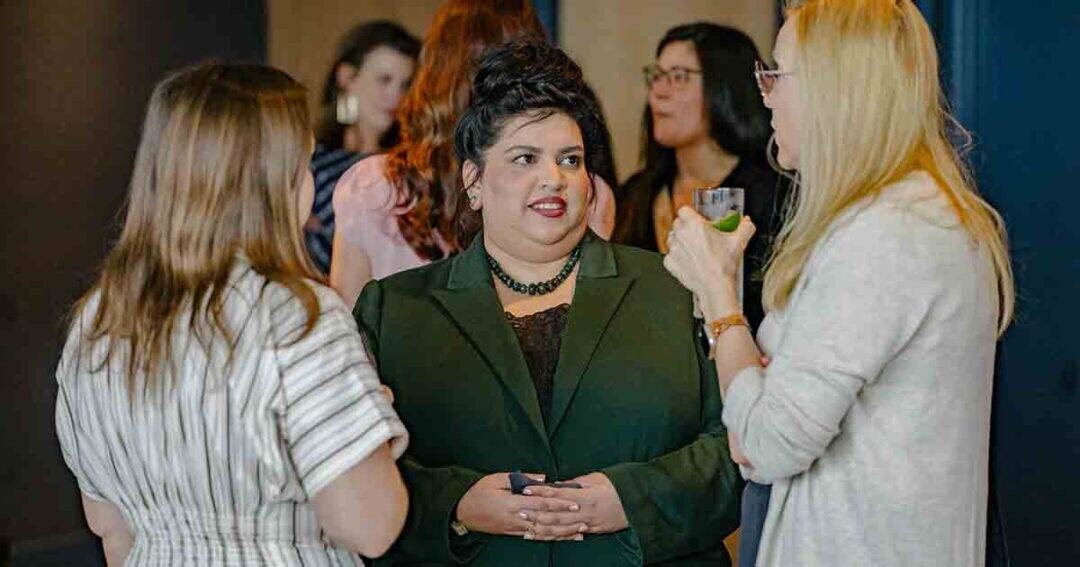 Allergy & Asthma Day Capitol Hill 2025: Leading the Charge Amid Federal Policy Shifts 25 A group of women are standing and talking at an indoor event. The woman in the center wears a dark green blazer, while others around her are engaged in conversation, one holding a drink.