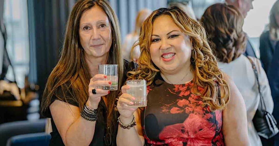 Allergy & Asthma Day Capitol Hill 2025: Leading the Charge Amid Federal Policy Shifts 24 Two women smiling and holding drinks, posing together at an indoor social gathering with other people in the background.