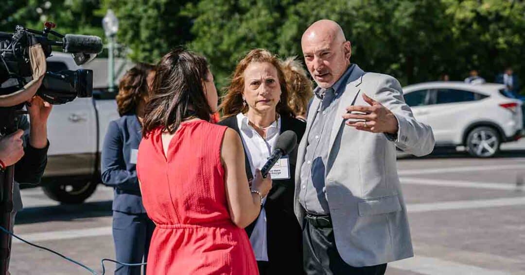 Allergy & Asthma Day Capitol Hill 2025: Leading the Charge Amid Federal Policy Shifts 13 A woman in a red dress interviews two people outdoors while a cameraman films. The man gestures with one hand, and cars and trees are visible in the background.