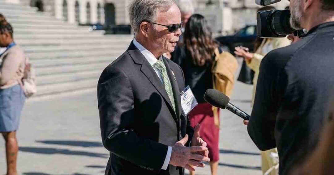Allergy & Asthma Day Capitol Hill 2025: Leading the Charge Amid Federal Policy Shifts 4 A man in a suit and sunglasses is being interviewed outdoors by a person holding a microphone and a video camera, with several people and steps visible in the background.