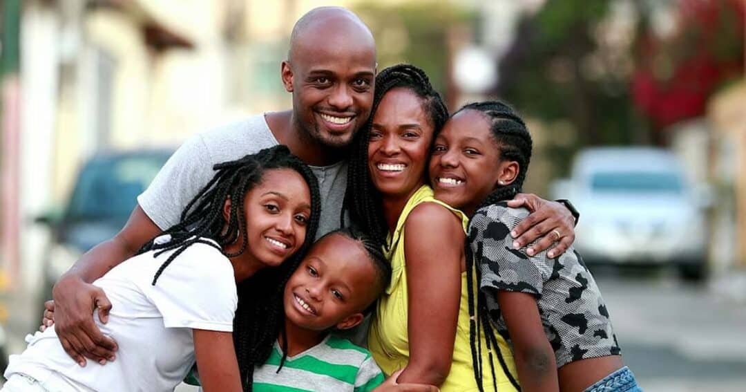 Resources for Care and Support 7 A happy family of five, including two adults and three children, stands closely together outdoors. They are all smiling, with warm expressions, in a casual setting with blurred buildings in the background.