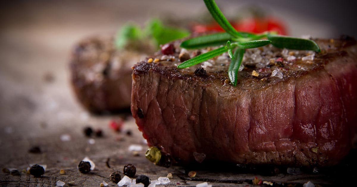 close-up of a cooked steak topped with rosemary and peppercorns