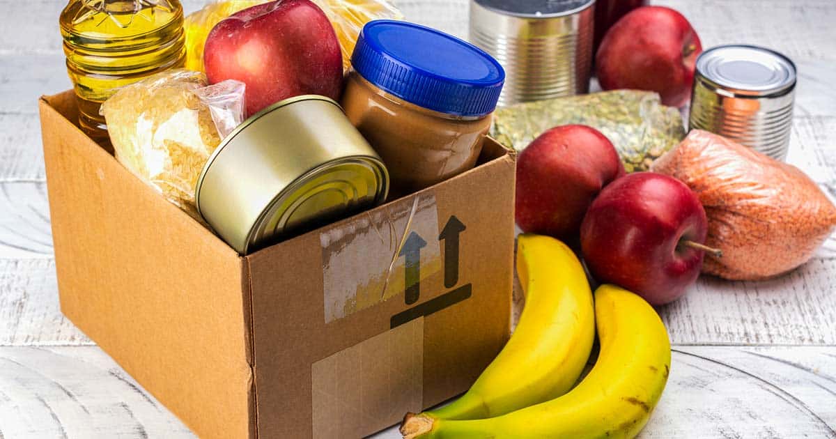 What Can You Do If You Can’t Afford Allergen-Free Foods? 3 food from a pantry program. box and table filled with fruits, dry goods, and canned goods.