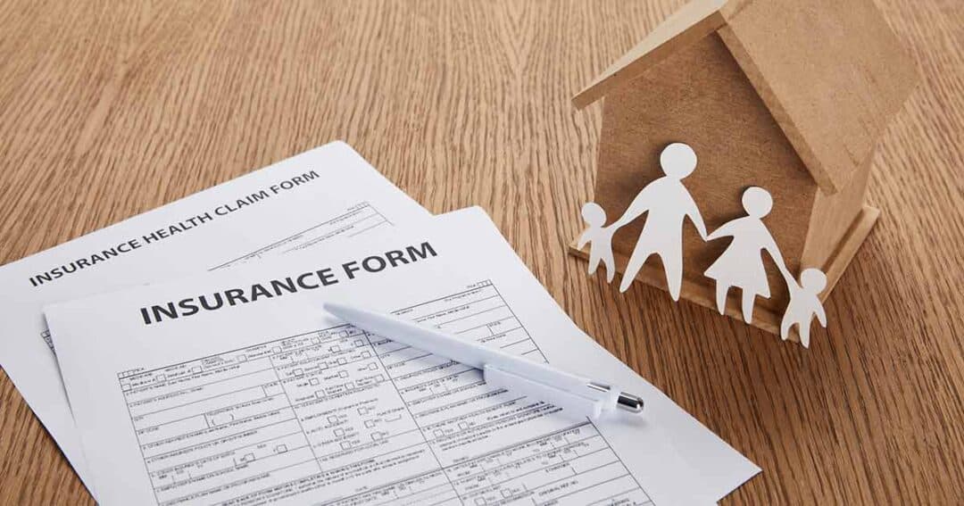 insurance form on table next to a paper cutout family leaning on a small wooden home