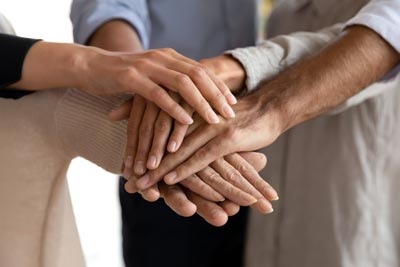 Ways to Give 4 A group of people stacking their hands together in a gesture of teamwork and unity. The image focuses on the hands overlapping each other, symbolizing collaboration and mutual support.