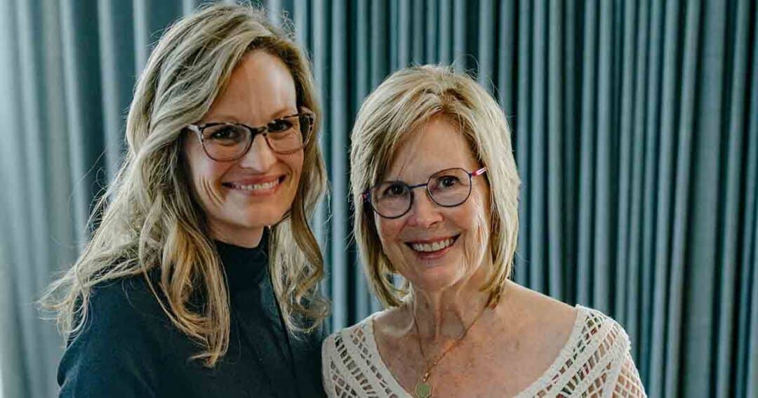 Allergy & Asthma Day Capitol Hill 2025: Leading the Charge Amid Federal Policy Shifts 36 Two women with blonde hair and glasses smile at the camera while standing close together in front of grey curtains. One wears a black top; the other wears a white, patterned blouse.