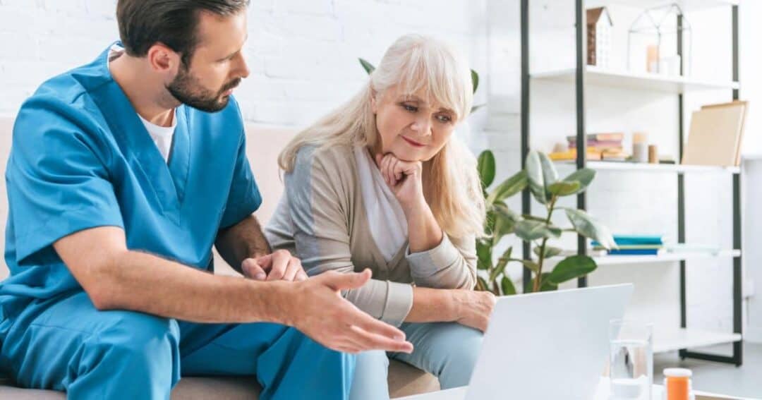 How can Patients and Caregivers Get Involved in Research? 4 A male nurse in blue scrubs is sitting on a couch and discussing something with an elderly woman with long white hair. They are looking at a laptop screen and he's helping her complete a survey. There is a plant and a shelf in the background.