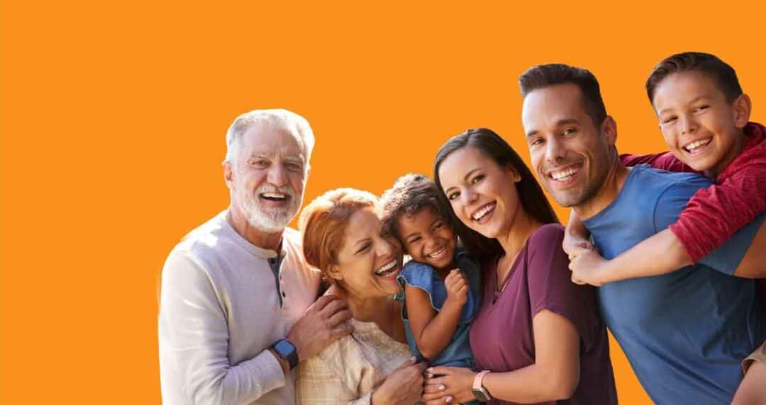 A group of six people, including three adults and three children, smile and pose together in front of an orange background. They appear joyful and are dressed casually.