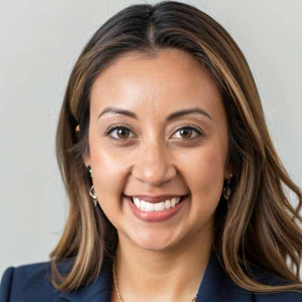 Smiling woman with long brown hair wearing a navy blazer. Neutral background.