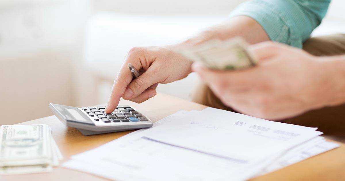 Resources for Care and Support 1 A person calculating expenses with a calculator and holding cash. There are papers and dollar bills on the table, indicating financial planning or budgeting activities.