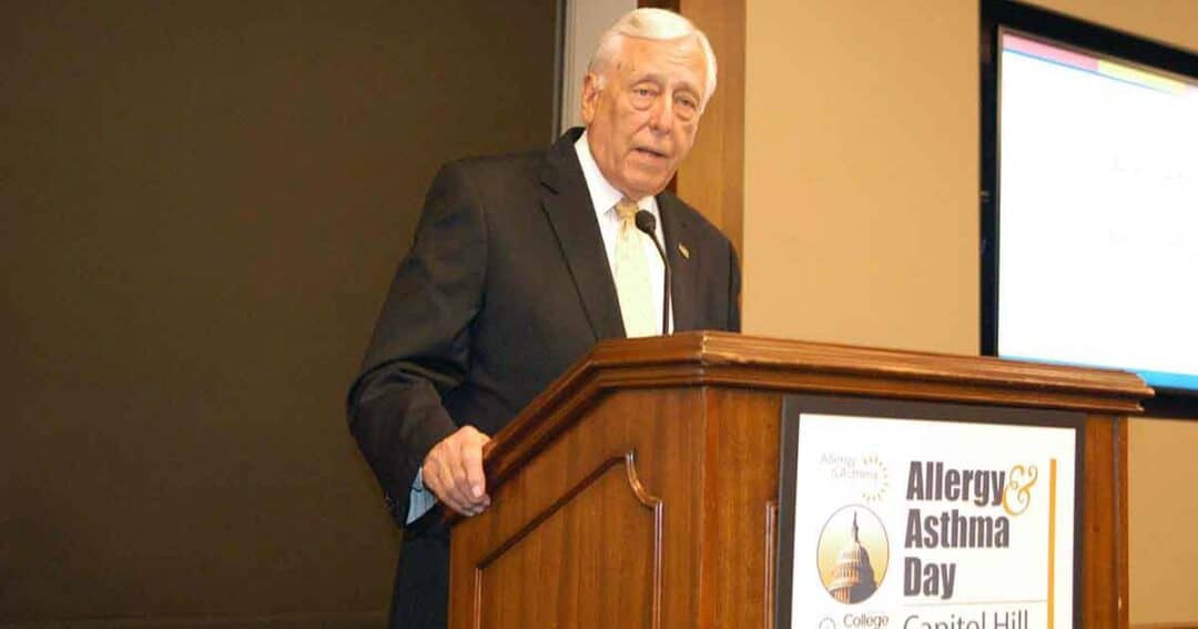 Steny Hoyer speaks at a podium labeled &ldquo;Allergy & Asthma Day on Capitol Hill.&rdquo; A projection screen and brown walls are in the background.