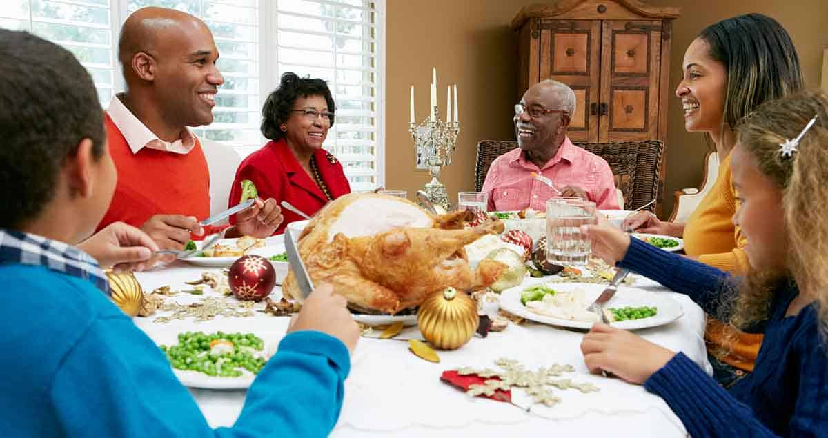 What Can You Do If You Can’t Afford Allergen-Free Foods? 4 A family gathered around a dining table enjoying a holiday meal. The table is set with a roast turkey, decorative ornaments, and side dishes. Everyone is smiling and engaging in conversation.