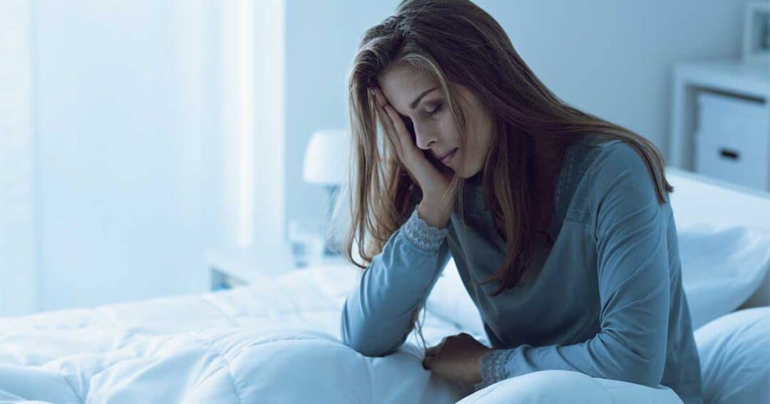 What is Nocturnal Asthma? 1 In the blue-lit room, a woman sits on her bed, resting her head with a tired expression. Wearing a long-sleeved top, she appears to be exhausted from lack of sleep because of night time asthma.